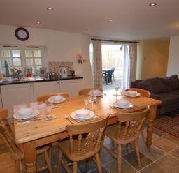 A kitchen and dining area with a wooden table set for six people next to a sofa and sliding doors at The Barn in Tregoodwell