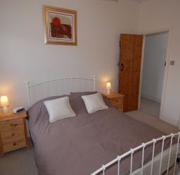 A bedroom with a double bed with gray bedding two bedside tables two lamps and wooden doors at The Barn in Tregoodwell