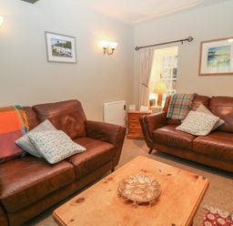 A sitting room with two brown leather sofas a wooden coffee table and a side table with a lamp at Robyn Cottage in Otterton