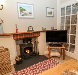 A corner with a wood burning stove fireplace a TV on a wooden table a wicker basket and framed paintings at Robyn Cottage in Otterton