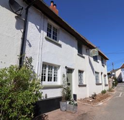 A white cottage with a thatched roof and plants outside along a street at Robyn Cottage in Otterton