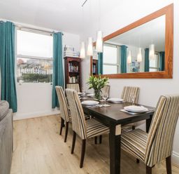A dining room with a dark wood table set for six with striped chairs a large mirror on the wall and teal curtains at Quayside Lookout in Brixham