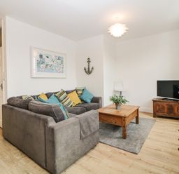 A living room with a gray sofa and colorful cushions a wooden coffee table a television on a wooden stand and a decorative anchor on the wall at Quayside Lookout in Brixham