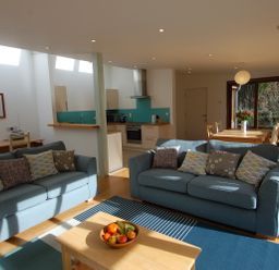 A living room with two blue sofas and a coffee table with fruit a kitchen with turquoise backsplash and a dining table with flowers at Orchard Retreat in Sidmouth