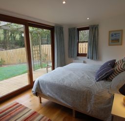 A bedroom with a bed pillows bedside table lamp sliding glass door and window at Orchard Retreat in Sidmouth