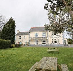 A large house with a covered porch and garden furniture on a lawn at Muriau Park in Caernarfon