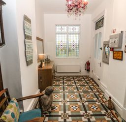 A hallway with patterned tiled floor a wooden chair a statue a dresser a lamp and stained glass window at Muriau Park in Caernarfon