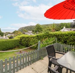 A garden with a table and chairs under an umbrella at 2 Argoed Llanbedrog
