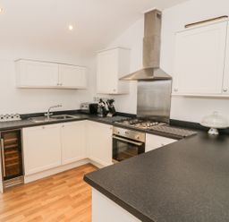 A kitchen with white cabinets black countertops a stainless steel oven gas stove and extractor fan a stainless steel sink a microwave and a wooden floor at 7 Marina View in Pwllheli
