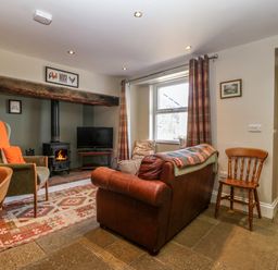 A living room with a leather sofa an armchair a wood-burning stove and a television at Trefollwyn Mawr in Abersoch