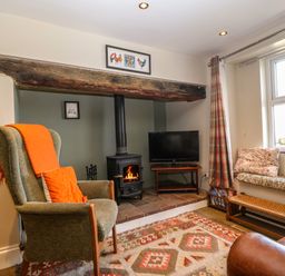 A living room with a green armchair and orange pillow next to a wood stove and television by a window with a bench seat at Trefollwyn Mawr in Abersoch