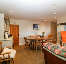 A dining area with wooden chairs around a table a hutch and an armchair with orange cushions at Trefollwyn Mawr in Abersoch