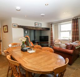 A dining area with a wooden table and chairs next to a seating area with a leather sofa a high back chair and a wood burning stove at Trefollwyn Mawr in Abersoch