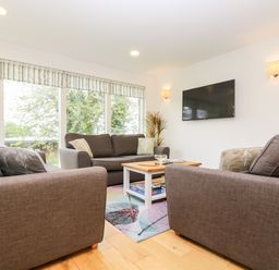 A living room with three gray sofas a wooden coffee table a wall mounted television and large windows at Beech in Truro
