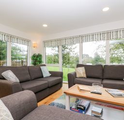 A living room with brown sofas a wooden coffee table and large windows showing greenery at Beech in Truro