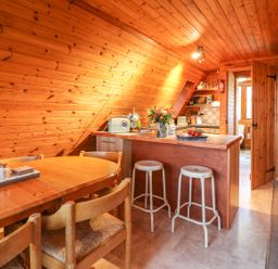 A wooden dining table with chairs and a kitchen counter with stools in a wooden room at Rose Lodge in Milton on Stour