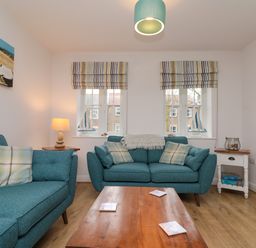 A living room with two teal sofas a wooden coffee table and two windows with striped roman blinds at Dotty's Sunshine Cottage in The Bay near Filey