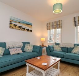 A living room with two teal sofas a wooden coffee table a table lamp and wall art of boats at Dotty's Sunshine Cottage The Bay near Filey