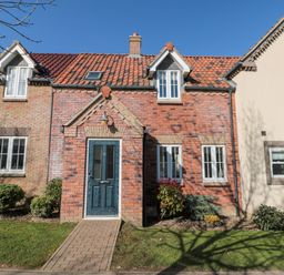 A brick house with a blue front door and windows with white frames surrounded by shrubs at Dotty's Sunshine Cottage The Bay near Filey