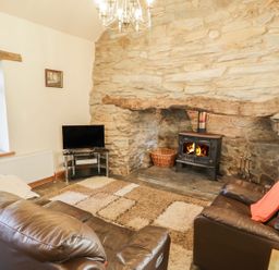 A living room with leather sofas a wood stove in a stone fireplace and a television at Yr Hen Dy in Llan Ffestiniog