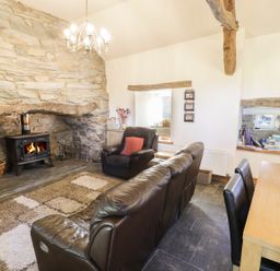 A living room with a stone fireplace wood stove leather sofa and armchair a wooden dining table and chairs at Yr Hen Dy in Llan Ffestiniog