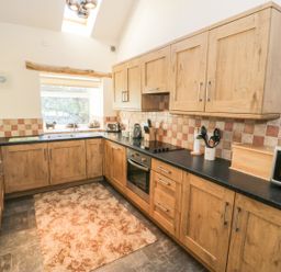 A kitchen with wooden cabinets and black countertops with a window above the sink at Yr Hen Dy in Llan Ffestiniog