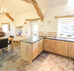 A kitchen and dining area with wooden beams on the ceiling at Yr Hen Dy in Llan Ffestiniog