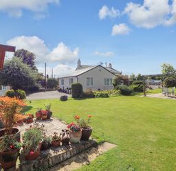 A garden with potted plants a white house and a patio with chairs and table at The Flat At Brwyn in Brynford
