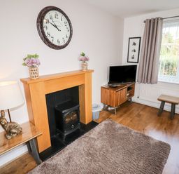 A living room with a fireplace clock TV rug and window at The Flat At Brwyn in Brynford