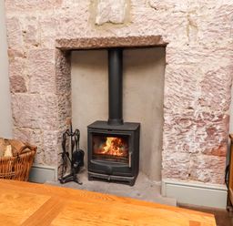 A fireplace with a wood stove and a basket of firewood at Gamekeepers Cottage in Chillingham near Chatton