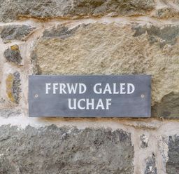 A stone wall with a rectangular gray sign reading Ffrwd Galed Uchaf at Ffrwdd Galed Uchaf in Tregarth