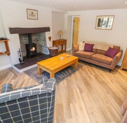 A living room with a fireplace a wooden coffee table two brown sofas a checkered armchair and a wooden cabinet at Ffrwdd Galed Uchaf in Tregarth