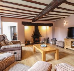 A living room with wooden beams on the ceiling a wood burning stove sofas a wooden coffee table and a television on a wooden stand at Rhydygaled in Llanrhaeadr-Ym-Mochnant