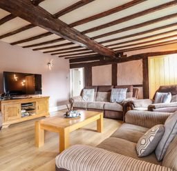 A living room with wooden beams on the ceiling sofas a wooden coffee table and a television on a wooden stand at Rhydygaled in Llanrhaeadr-Ym-Mochnant