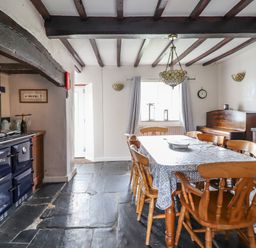 A dining room with a table and wooden chairs next to a piano and a stove at Rhydygaled in Llanrhaeadr-Ym-Mochnant