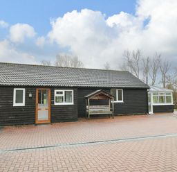 A black wooden building with a tiled roof and a paved area in front at The Annex in Royal Wootton Bassett