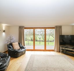 A living room with leather armchairs a television on a stand and sliding glass doors opening to a garden at The Annex in Royal Wootton Bassett