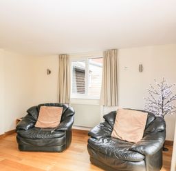 A room with two black leather armchairs each with a brown cushion and a window with beige curtains at The Annex in Royal Wootton Bassett