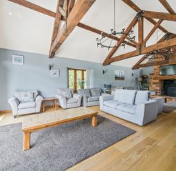 A living room with exposed wooden beams a fireplace and multiple sofas at The Old Byres in Washford near Watchet