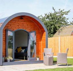A wooden pod with open glass doors showing a sofa inside and two patio chairs with a table outside at Withy Willows Diddlebury near Ludlow