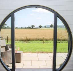 A circular window opening to a patio with chairs and drinks overlooking a field at Withy Willows in Diddlebury near Ludlow