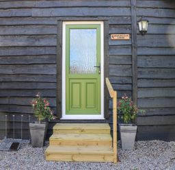 A green door with frosted glass on a wooden lodge with steps and two potted plants at Woodpecker Lodge in Henley near Langport