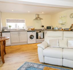 An open plan kitchen and living room with a white sofa and wooden dining table at Woodpecker Lodge in Henley near Langport