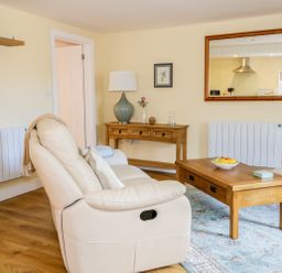 A living room with a cream sofa wooden coffee table with a fruit bowl a console table with a lamp and a mirror on the wall at Woodpecker Lodge in Henley near Langport
