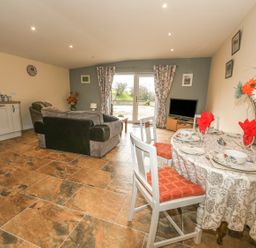 A living room with a dining table set with red napkins and floral dishes a sofa a television and kitchen cabinets at Knott Lodge in Sedbergh