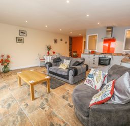 An open living room and kitchen with sofas, a wooden coffee table, a dining table with chairs, and kitchen appliances at Knott Lodge in Sedbergh