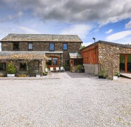 A stone house with a gravel courtyard and outdoor chairs at Knott Lodge in Sedbergh