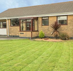 A front view of a single-story house with a lawn and small garden at Dehangfa in Fairbourne