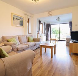 A living room with beige sofas wooden tables a television and sliding glass doors at Dehangfa in Fairbourne