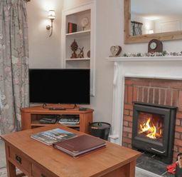 A living room with a wood burning stove beside a wooden coffee table and a television on a wooden stand at Kirkstone Cottage in Ambleside